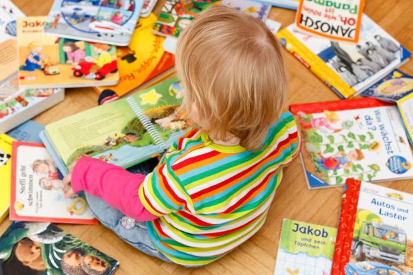 Kleines Kind sitzt mitten in bunten Büchern und blättert