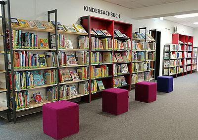 Kindersachbuchregal mit Hockern © Stadtbibliothek Kempen Eine lange Bücherwand mit Kinderbüchern, davor stehen 4 quadratische Stoffhocker