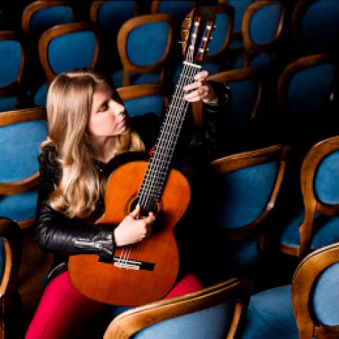 Laura Lootens spielt Gitarre in Reihen voller leerer Stühle