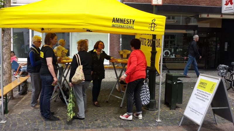 Informationsstand mit gelben Pavillon von Amnesty International. Menschen unterhalten sich